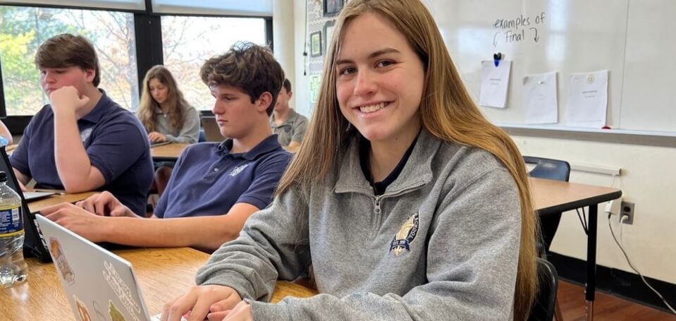 students working on laptops in a classroom; a female student smiles for the camera